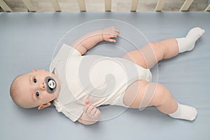 Cute infant lies in crib with pacifier in his mouth. Healthy sleep of newborn baby in wooden crib. Concept of maternity