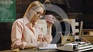 Cute intelligent clever concentrated girl is studying hard in class, writing down necessary information to her notebook