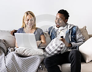 Cute interracial couple on a couch sharing laptop love, internet and music concept