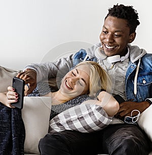 Cute interracial couple on a couch sharing smartphone love, internet and music concept