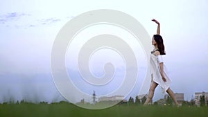 A cute Japanese girl in a white dress is engaged in ballet on green grass, slow motion