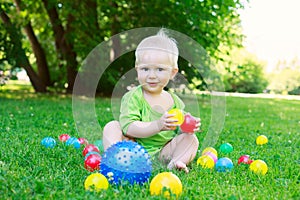 Cute kid baby boy sitting on grass playing with balls