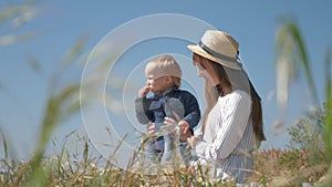 Cute kid boy eats lemon and grimaces during family picnic in nature sitting by mother in arms close up in meadow