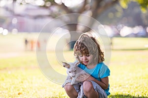 Cute kid boy feels delighted, carries little puppy dog, expresses tender emotions, Child care and love to small doggy