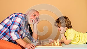 Cute kid boy with grandfather playing chess together at home. Childhood and board logic games. Grandpa and grandson play