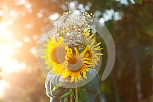 Cute kid boy hiding by bouquet of fields sunflowers in autumn sunset day. Autumn concept. Mothers day and thanksgiving concept