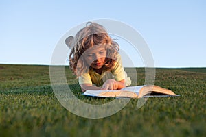 Cute kid boy reading book on green grass. Funny child reading the book in spring park.