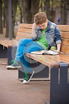 Cute kid boy sitting on a bench in the park and reading a book. Child learning and reading outdoors. School boy with a book