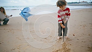 Cute kid drawing sand on autumn seaside. Happy family play having fun together