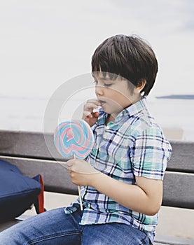 Cute kid eating lollipop, Happy little boy holding big sugar candy, Child with smiling face eat sweets, Active childhood enjoying