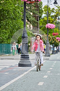 Cute kid girl in blue helmet going to ride her bike
