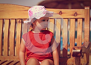 Cute kid girl in hat sitting on the bench on the beach