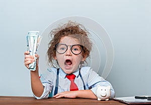 Cute kid girl holding dollars and have an idea how earning much money in crisis. Serious child teaching in eyeglasses