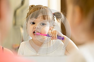 Cute kid girl looking at mirror using toothbrush cleaning teeth in bathroom every morning and night.