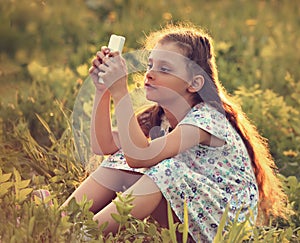 Cute kid girl sitting on the glass and playing on mobile phone w