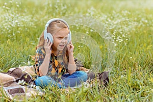 cute kid listening music in headphone while sitting on blanket in field