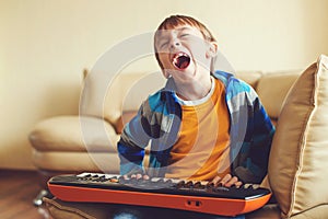 Cute kid playing on synthesizer at home. Boy learning to play musical instruments