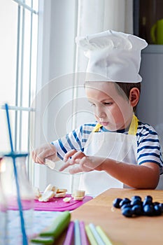 Cute kid preparing a fruit salad in kitchen