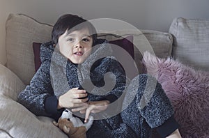 Cute kid sitting on sofa holding remote control, A happy child boy relaxing at home watching TV during cold weather outside in
