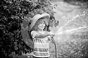 Cute Kid in straw hat is laughing with water spraying hose