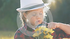 Cute kid tourist examines the plant through a magnifying glass on the grass in the park. Baby girl through a magnifying