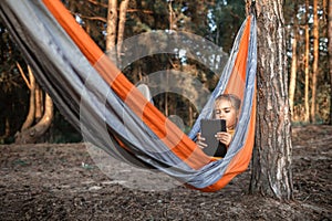 Cute kid using digital gadget for reading and learning in hammock, online education