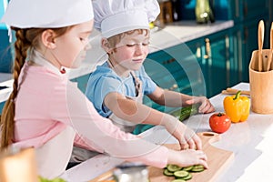 cute kids in chef hats and aprons preparing vegetable salad together