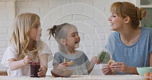 Cute kids daughters and happy mom eating cookies in kitchen