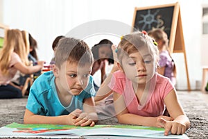 Cute kids reading book on floor while other children playing together