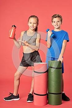 Cute kids with sports equipment standing against red background