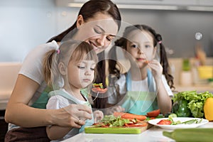 Cute kids tasting vegetables as they prepare a meal with their mother in the kitchen