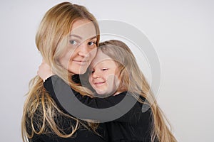 Cute kind caucasian blonde mom and daughter posing on white background. a parent and a child experience love and hug.
