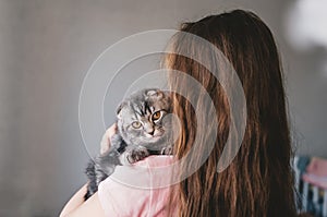 Cute kitten sits on the long-haired little girl`s shoulder and looks to camera