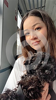 Cute Korean woman holding black poodle puppy sitting in train on railway trip. Traveling with dog. Asian female person