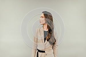 Cute lady in a beige suit stands on a beige background and looks away. Copy space
