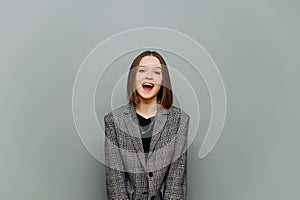 Cute lady in a jacket stands on a gray background with a happy face and poses for the camera. Portrait of a young positive