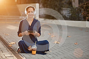 Cute lady surf using tablet. Girl in headset listen music sit on ground. Coffee break and leisure time idea, copy space