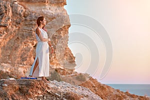 Cute lady in white dress posing on rock. Sunset over sea and nature. Contemplation and self absorbed idea, copy space