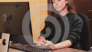 Cute lady working at computer in office. A girl with black nails in a black dress is typing text on a black keyboard and