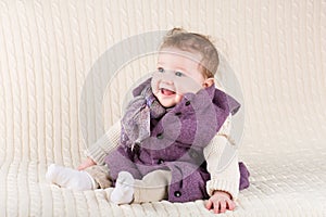 Cute laughing baby girl in purple jacket on knitted