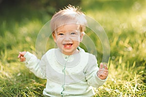 Cute laughing blonde baby girl 1 year old wear knit sweater top having fun sitting in green grass