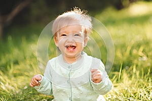 Cute laughing blonde baby girl 1 year old wear knit sweater top having fun sitting in green grass