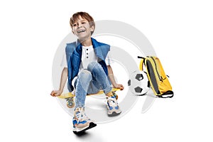 Cute laughing blonde boy sitting on yellow skateboard on white background. Back to School.