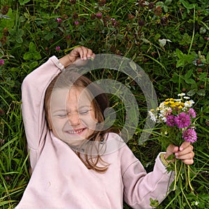 A cute laughing little girl, laying on the grass and taking a bouquet of field flow