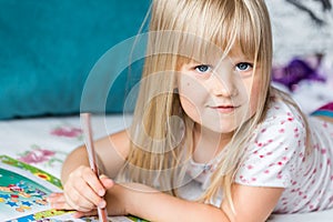 Cute liitle blonde girl lying on a bed and making homework