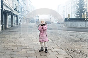 Cute liitle sad lost caucasian girl in warm long pink jacket and hat feel horror on empty street of old european city