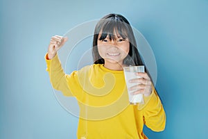 cute litle girl drinking milk in glass with smiling happy on blue