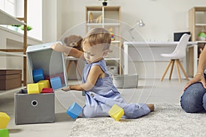 Cute little 2 year old child putting toys back in their place, helping mommy to tidy up