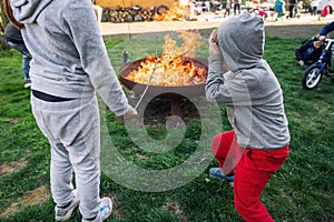 Cute little adorable baby and girl put big wooden stick in fire pit with huge fire at house garden yard. Child play