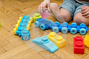 Cute little adorable caucasian boy playing with multi-colored constructor at home. Babys hands building tower of plastic